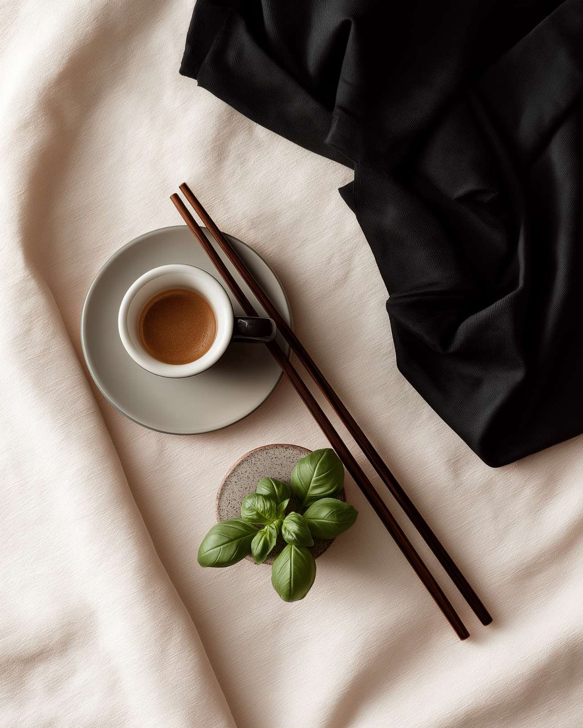 Black tee, espresso and basil on cream fabric, minimal still-life, FIOR