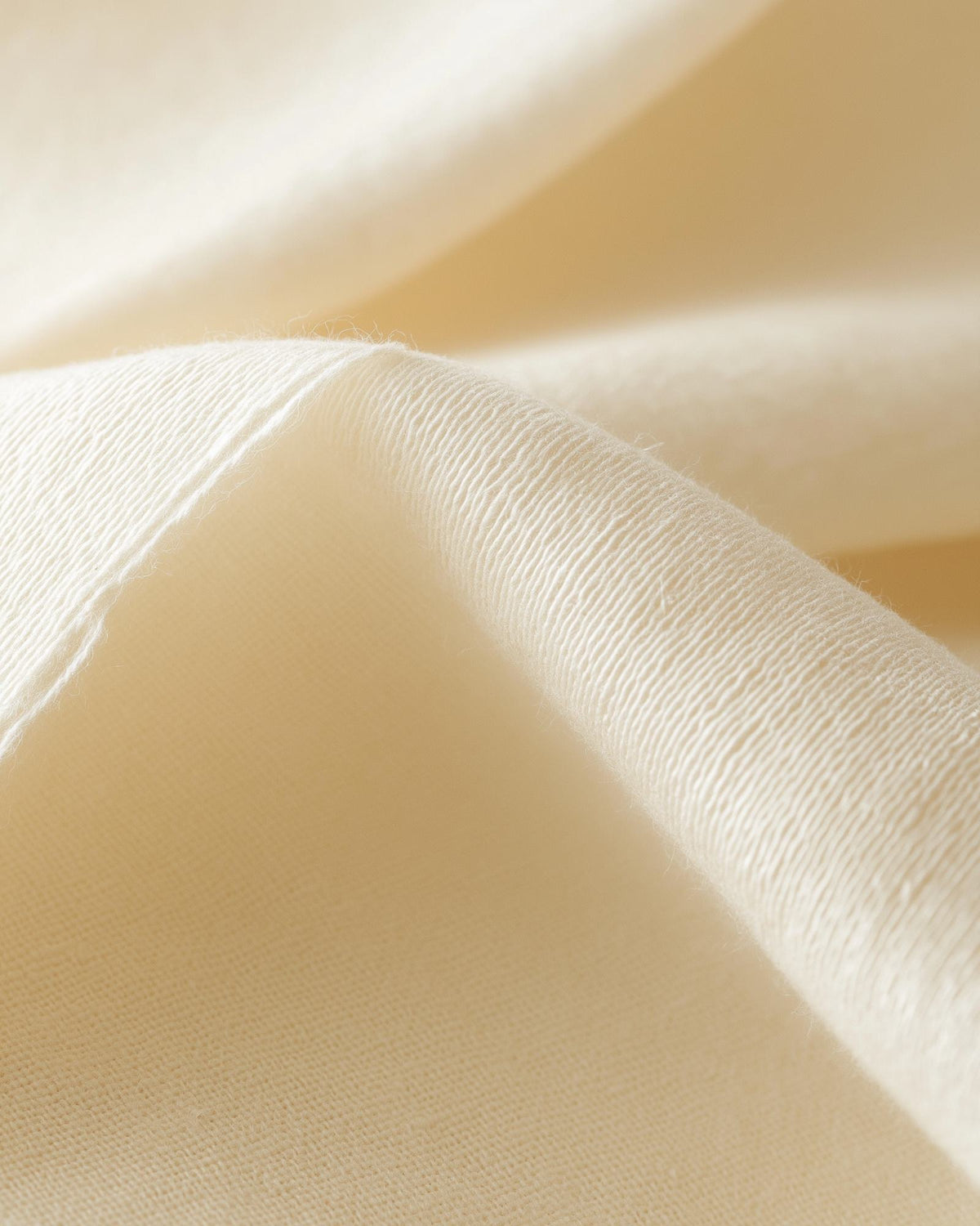 Macro folds of cream organic cotton in soft daylight, FIOR.