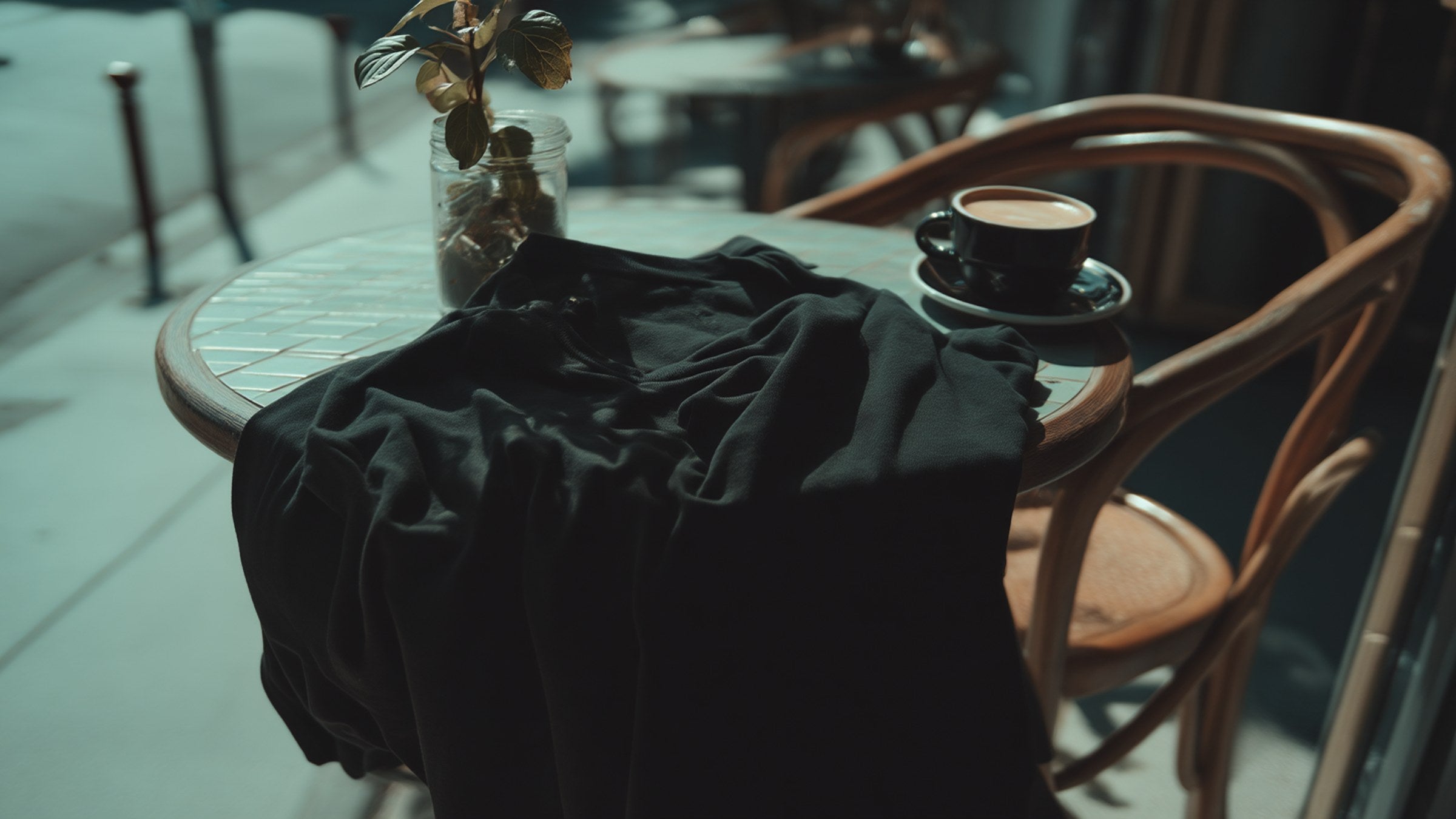 Lookbook banner: black tee draped on café chair with espresso, soft street bokeh, FIOR.