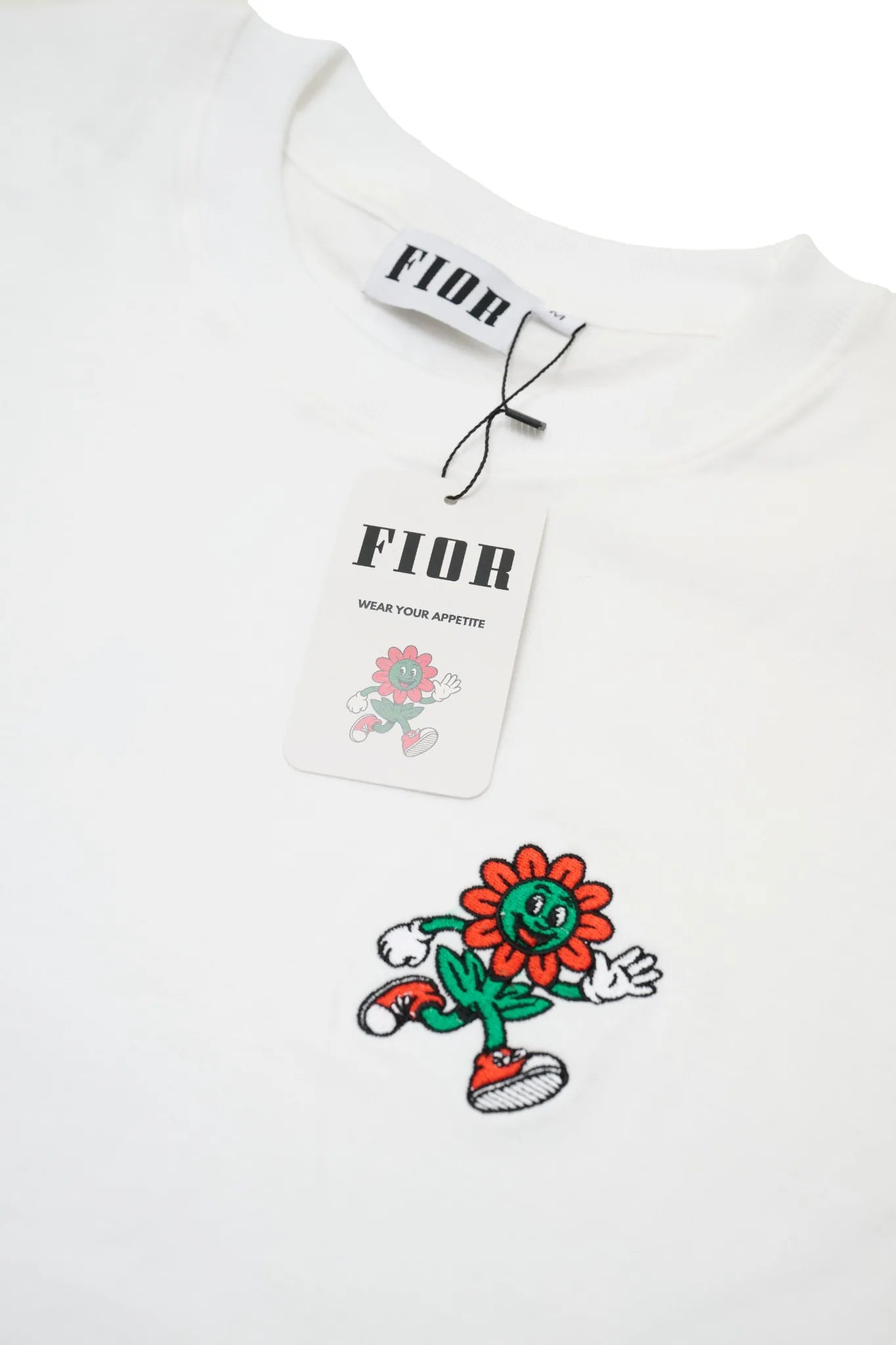 Cartellino FIOR e ricamo mascotte su T-shirt bianca, dettaglio branding