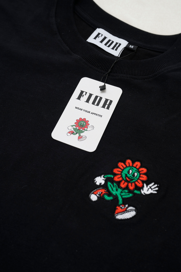 Cartellino FIOR e ricamo mascotte su T-shirt nera, dettaglio branding