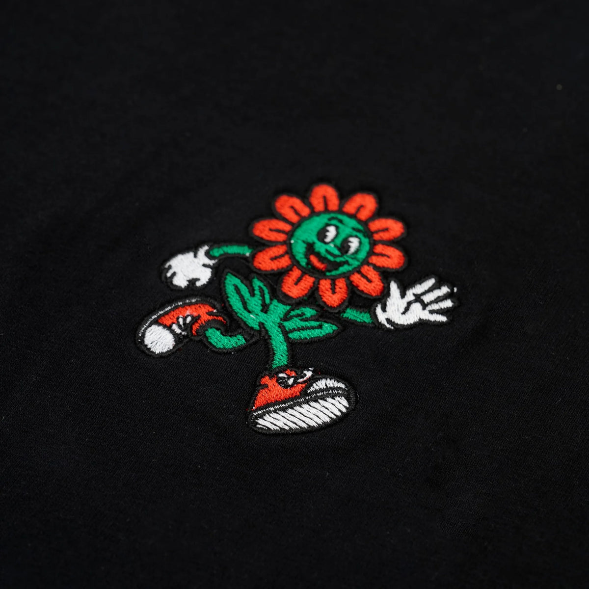Ricamo mascotte FIOR a colori su T-shirt nera, primo piano della texture del cotone.